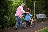 Foto: Ein älterer Herr in einem pinken Shirt schiebt ein Mädchen auf einem Fahrrad an