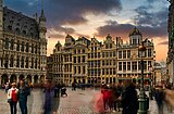 Menschenmenge auf dem gepflasterten Platz in Brüssel vor historischen barocken Gebäuden bei Sonnenuntergang mit dramatischem Himmel