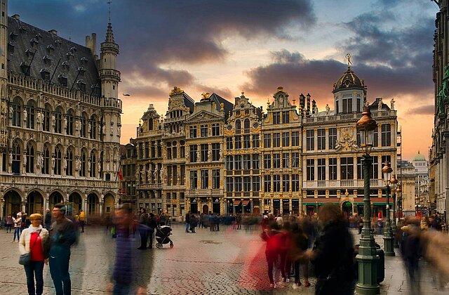Menschenmenge auf dem gepflasterten Platz in Brüssel vor historischen barocken Gebäuden bei Sonnenuntergang mit dramatischem Himmel