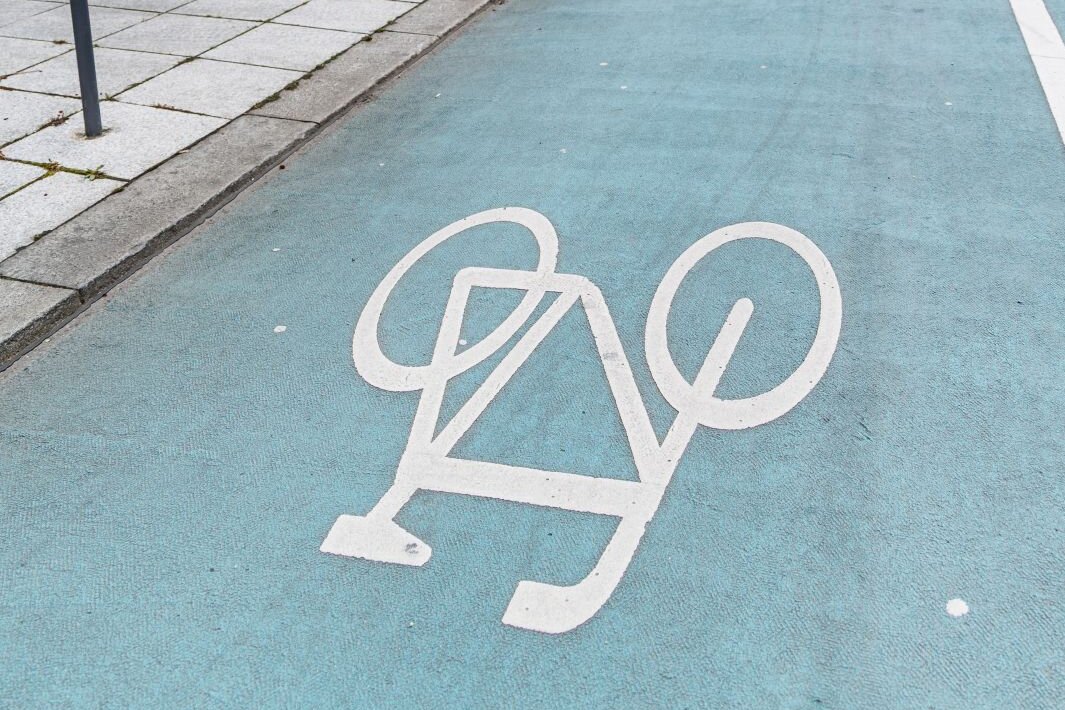 Gruppe von Menschen steht an einem blauen Radweg mit weißem Fahrradsymbol neben einer Straße in einer Stadt