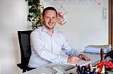 Florian Glock, Bürgermeister von Magstadt, sitzt hinter einem Schreibtisch und hält einen Stift in der Hand.
