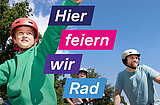 Drei Personen mit Fahrradhelmen auf Fahrrädern, eine Person zeigt mit ausgestrecktem Arm nach oben, blauer Himmel und Bäume im Hintergrund, Text 'Hier feiern wir Rad'
