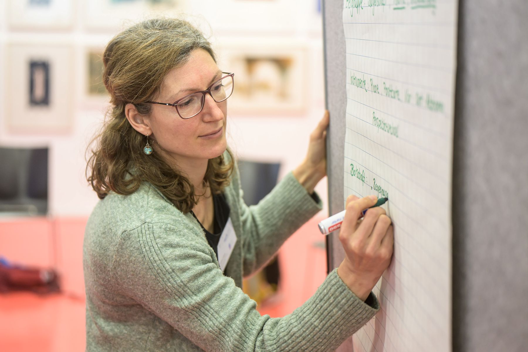 Frau mit Brille und grünem Pullover schreibt mit Marker auf ein Flipchart