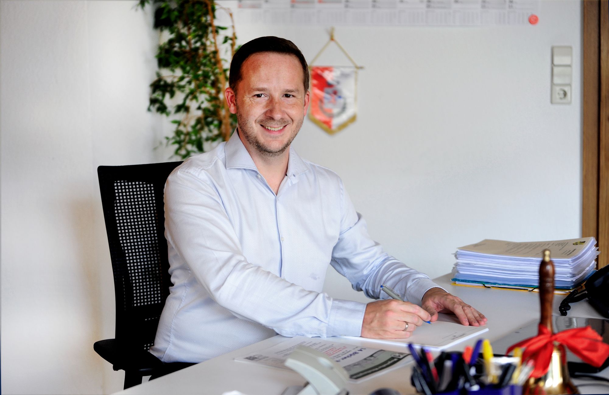 Florian Glock, Bürgermeister von Magstadt, sitzt hinter einem Schreibtisch und hält einen Stift in der Hand.