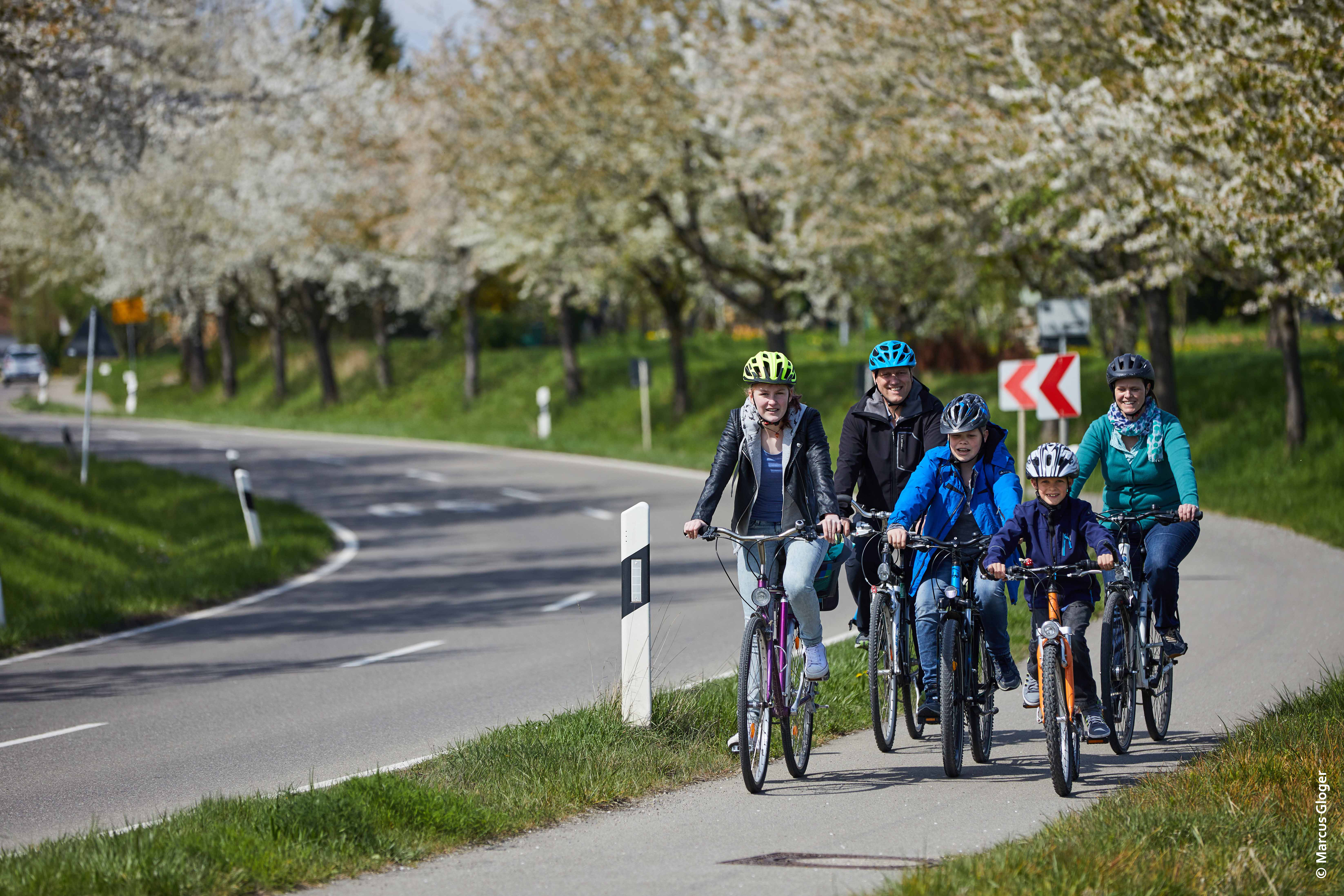 Eine Gruppe aus Erwachsenen und Kindern fährt auf einem getrennt von einer Bundesstraße geführten Radstreifen mit ihren Fahrrädern.