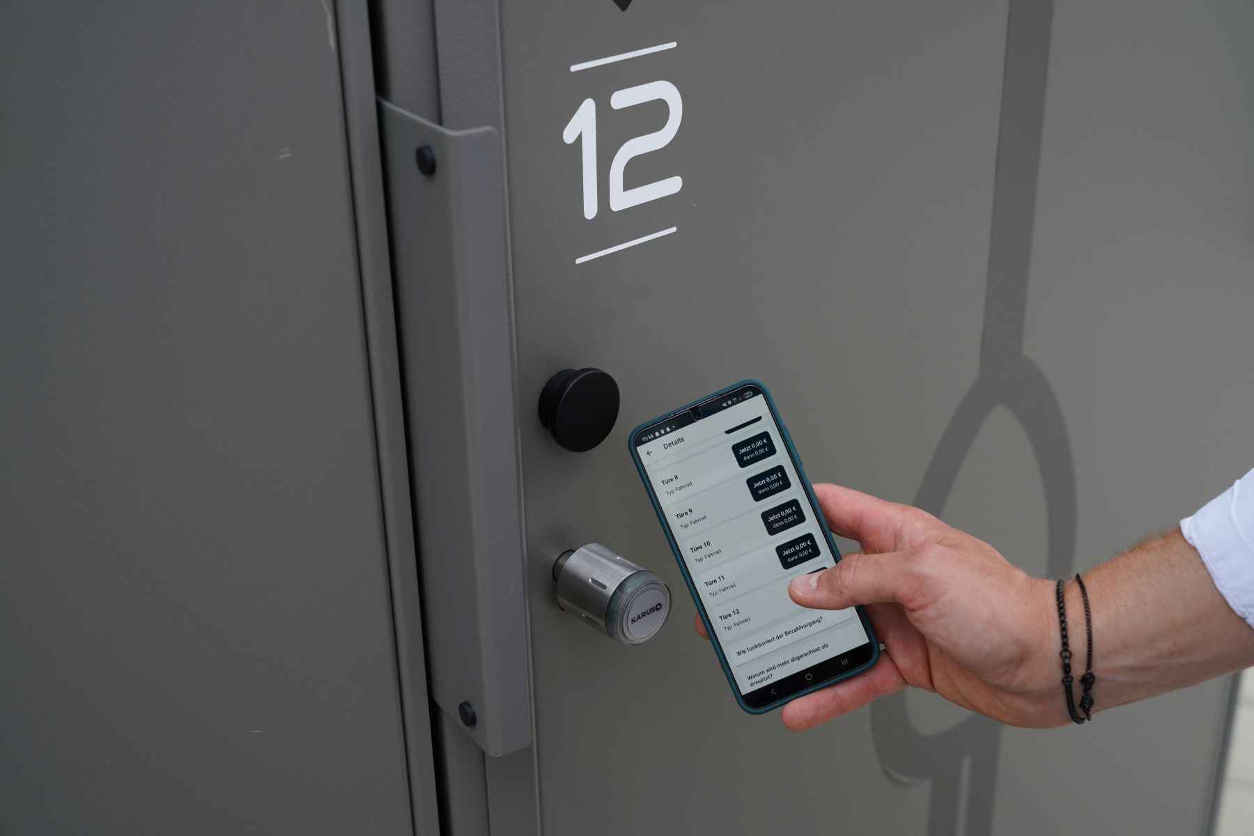 Hand hält Smartphone vor Tür mit der Nummer 12 und elektronischem Türschloss