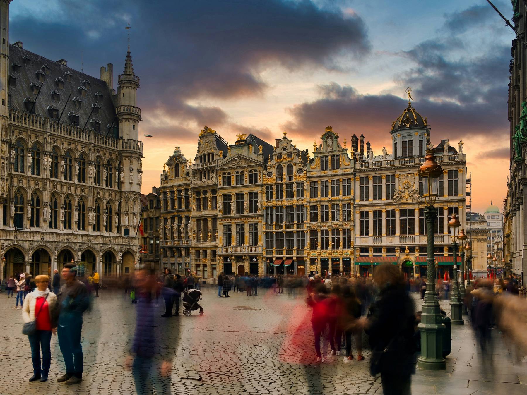 Menschenmenge auf dem gepflasterten Platz in Brüssel vor historischen barocken Gebäuden bei Sonnenuntergang mit dramatischem Himmel